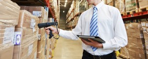 man in tie holding tablet and firing scan gun at boxes in warehouse