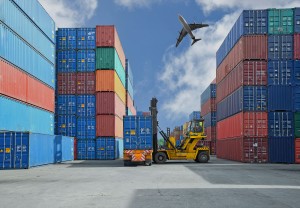 shipping yard with forklift lifting container onto truck and plane in the sky