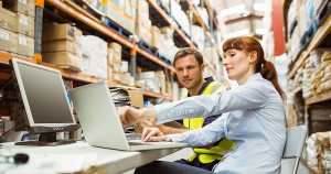 two workers in warehouse looking at laptop screen at table