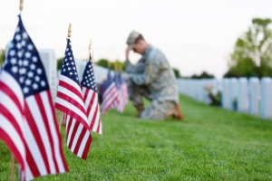 American soldier kneeling at a veterans grave on memorial day. Focus on the foreground.
