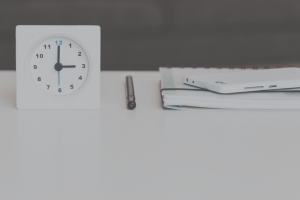 white table with white analog clock, black pen, notebook and white phone