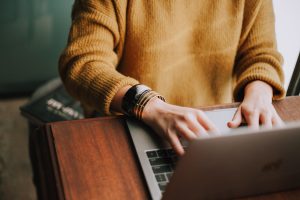 Women wearing a mustard knit shirt typing on her laptop